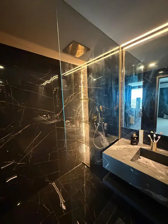 Baño de mármol negro con espejo, iluminación LED y mampara