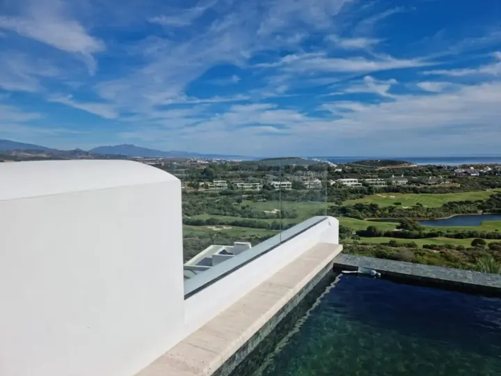 Barandilla de cristal en terraza con piscina y vistas al golf