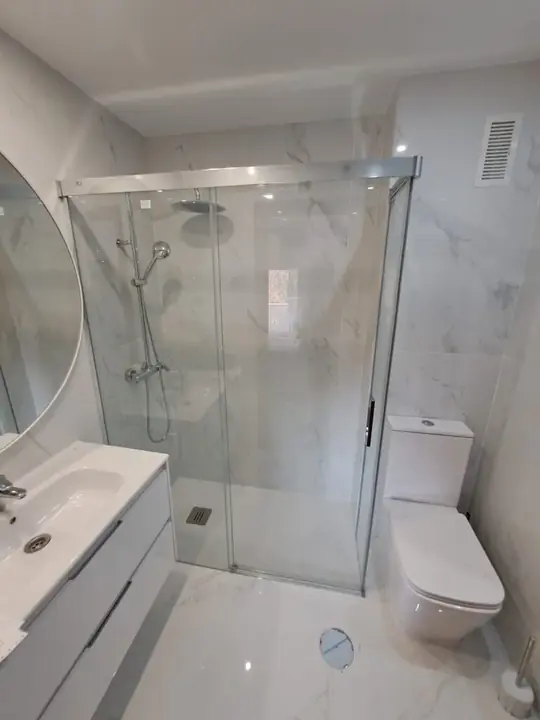 Mampara corredera de cristal en baño blanco de mármol