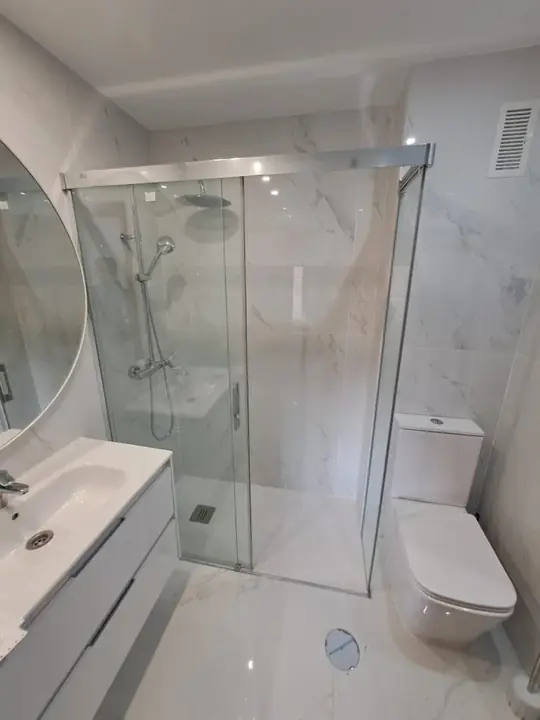 Mampara corredera de cristal transparente en baño de mármol