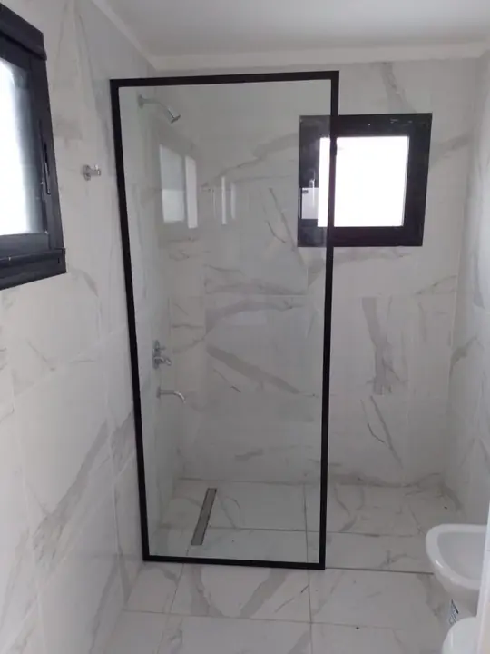 Mampara fija con perfil negro en baño de mármol blanco