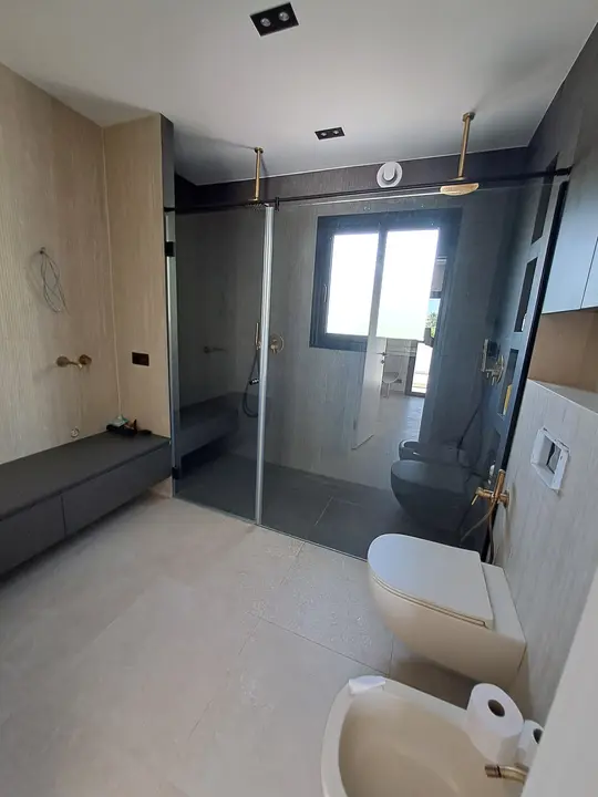 Mampara walk-in en baño gris con grifería dorada