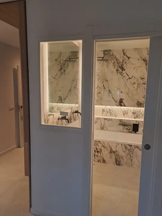 Ventana interior de cristal hacia baño de mármol